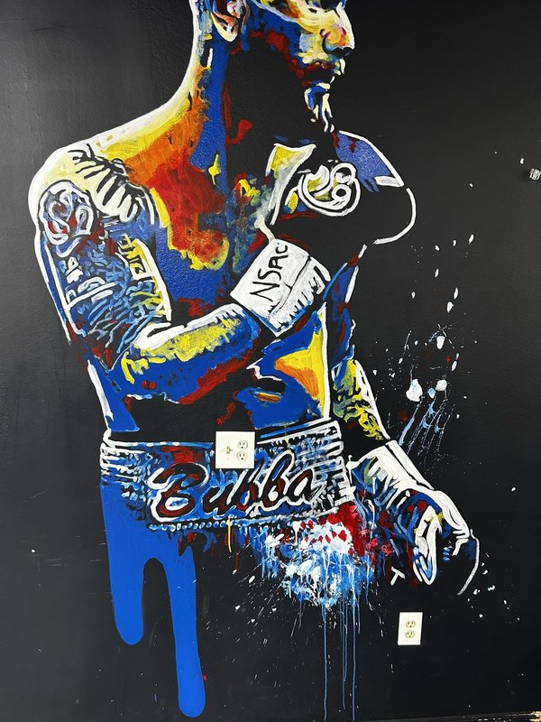 Hand-painted expressionist mural of a fighter named 'Bubba' painted in bold blues, yellows, and reds on a black wall