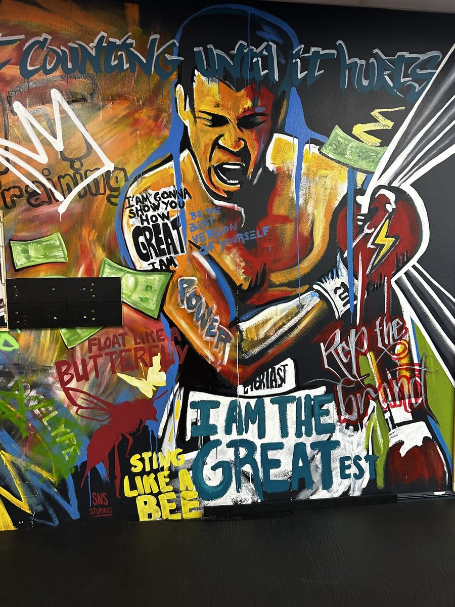 Hand-painted mural of a boxer with arms raised, surrounded by phrases including 'I AM THE GREATEST,' 'FLOAT LIKE A BUTTERFLY,' and 'STING LIKE A BEE'