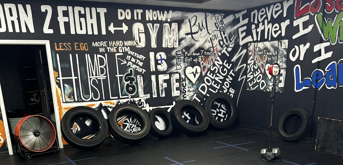 Hand-painted motivational typography covering the gym training wall: 'Born 2 Fight,' 'Hustle Is Life,' 'I never lose — either I WIN or I LEARN,' and other phrases
